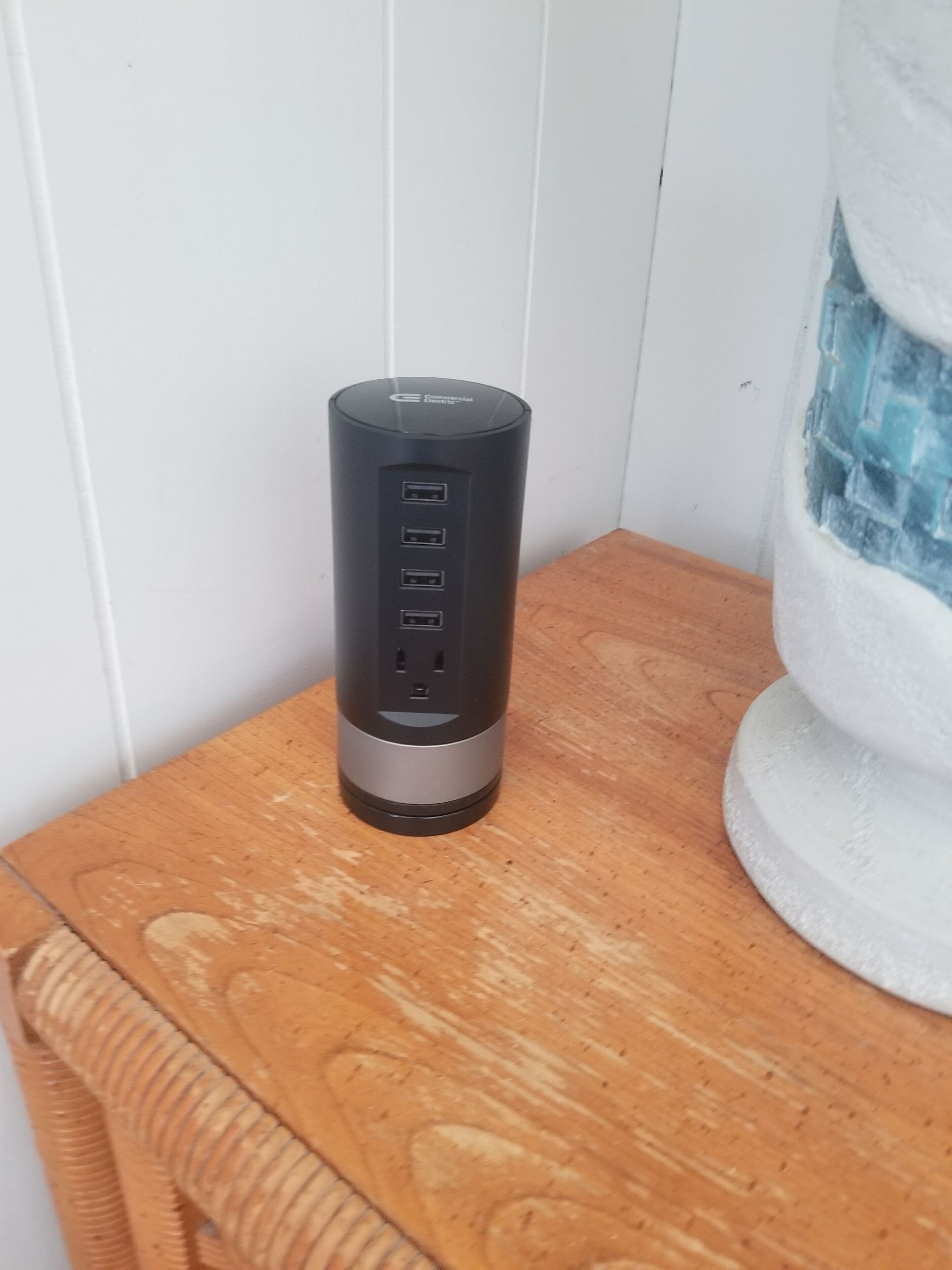 A black cylindrical device with four USB ports and a power outlet on a wooden surface.
