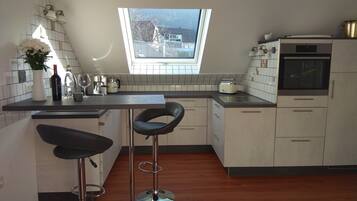 Eine moderne Küche mit Dachfenster, zwei Barhocker, einer Kaffeemaschine und einem eingebauten Backofen.