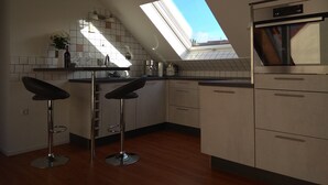 Une cuisine moderne dotée d’un puits de lumière, de deux tabourets de bar, d’une machine à café et d’un four encastré.