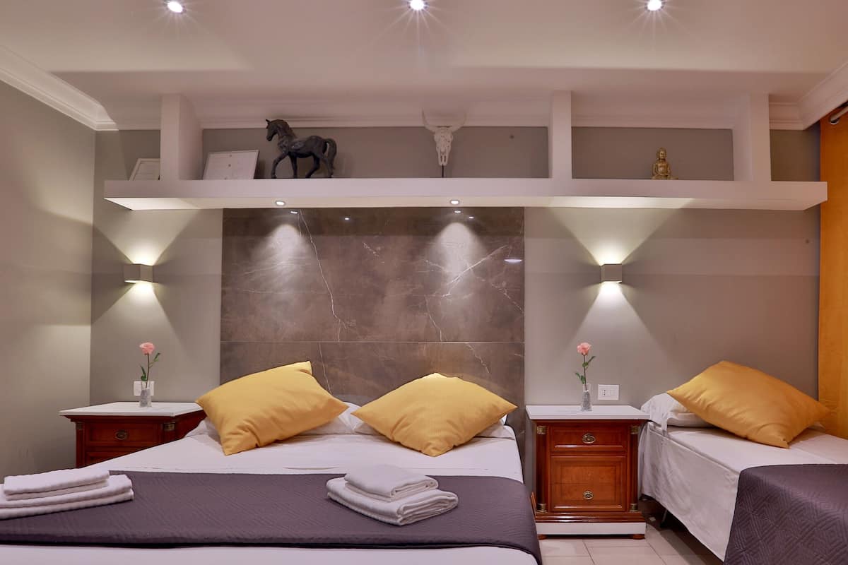 A hotel room with two beds, each with a yellow pillow, a marble headboard, and a small statue above the headboard.