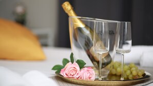Eine Champagnerflasche in einem Glas, zwei Gläser, ein Teller mit Trauben und eine pinkfarbene Rose auf einem Tablett.