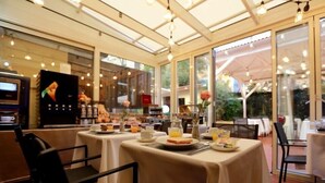 Ein Restaurant mit gedeckten Tischen für das Frühstück, einer Kaffeemaschine und Blick ins Freie.