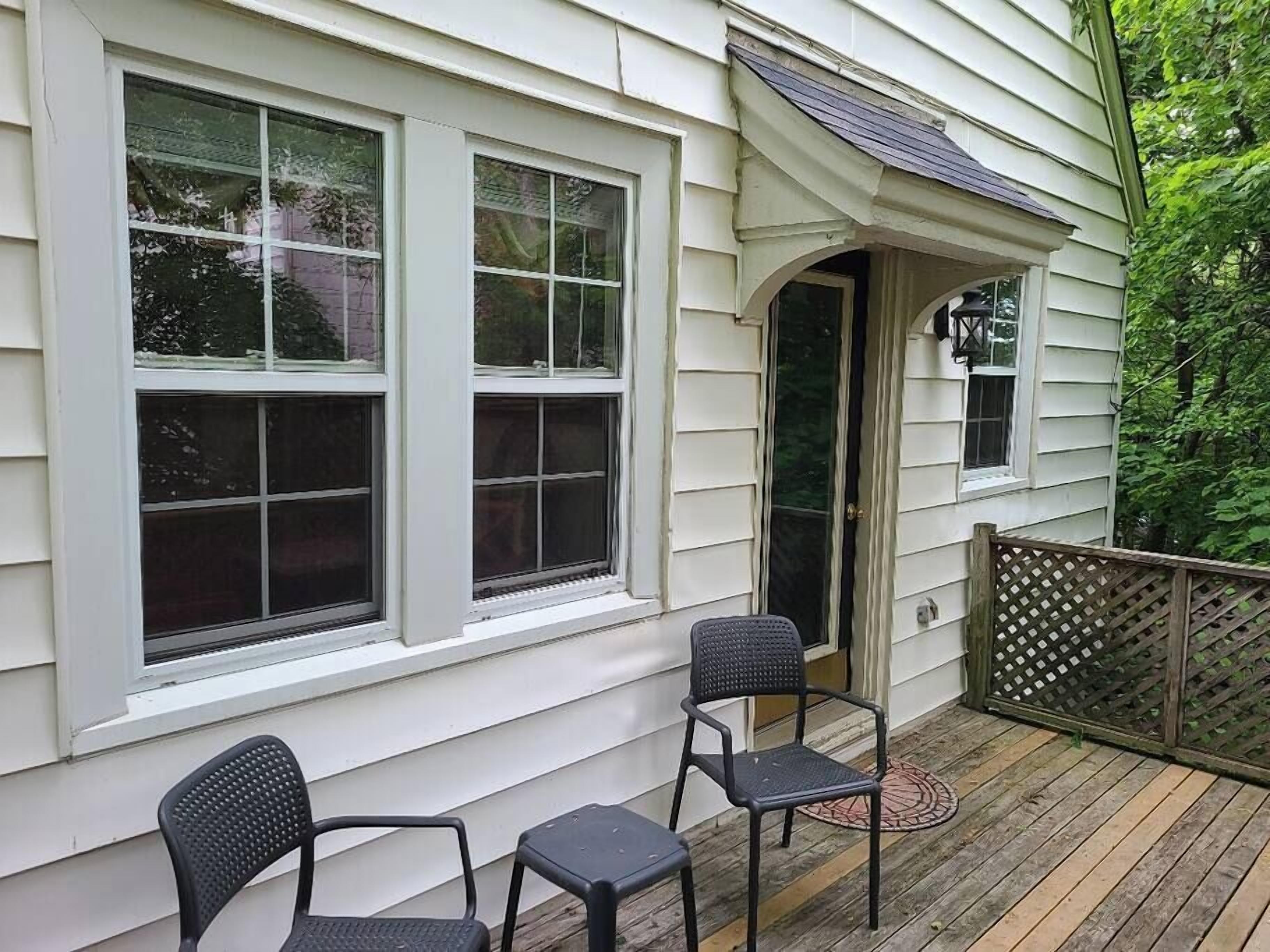 Eine Veranda mit zwei Stühlen und einem kleinen Tisch, weißes Holzverkleiden und einer Holzterrasse.