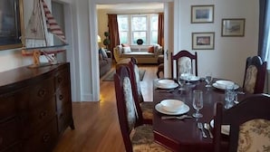 A dining room with a wooden table set for four, flanked by chairs with floral upholstery. A wooden cabinet with drawers is to the left. - 1930's Gingerbread Style - Ambience & Waterviews (Armdale)