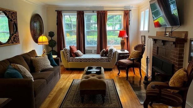 A living room with a sofa, armchairs, a coffee table, a fireplace, and a TV mounted on the wall. - 1930's Gingerbread Style - Ambience & Waterviews (Armdale)