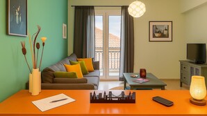Ein Wohnzimmer mit einer Couch, einem Tisch, einem Fernseher und einem Balkon mit Vorhängen.