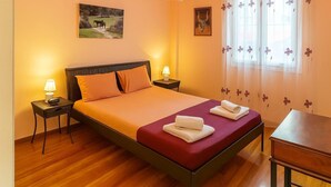 Ein ordentlich eingerichtetes Schlafzimmer mit einem Bett, zwei Nachttischen mit Lampen, Holzboden und einem Fenster mit blumigen Vorhängen.