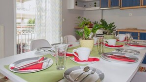 A dining area with a table set for four, including plates, cutlery, and glasses. There are potted plants on the table, and a window with curtains to the left.