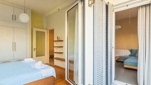 A bedroom with a bed, a wardrobe, a sliding glass door leading to a balcony, and a small seating area with a sofa. - Upscale Modern Escape in the Historic Center (Kalamata)