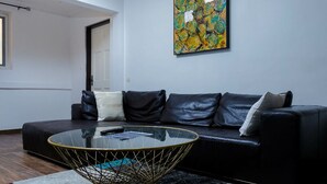 A modern living room with a black leather sofa, a glass coffee table with a wireframe base, and a colorful abstract painting on the wall. - The Key Boutique Hotel (Lomé)