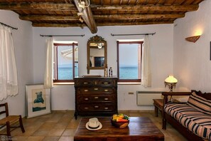 Una habitación con techo de madera, un espejo grande, un aparador, un sofá y vista al mar a través de dos ventanas.