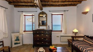 A room with a wooden ceiling, a large mirror, a dresser, a sofa, and a view of the sea through two windows. - Waveside Sanctuary - Luxurious Seastone Villa (Avia)