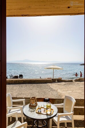 Mesa con sillas y sombrilla frente al mar.