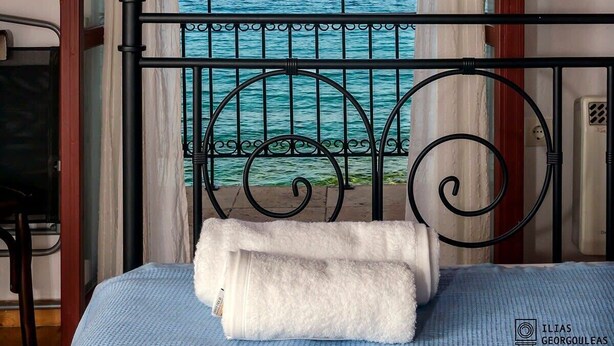 A room with a bed, a view of the sea, and a painting on the wall.