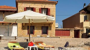 A stone building with a tiled roof, a white umbrella, and beach chairs.