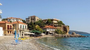 A coastal town with buildings on a hillside, a pebble beach, and clear blue water.