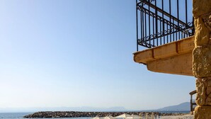 A seaside terrace with white chairs and a table, overlooking the sea and rocky shoreline. - Waveside Sanctuary - Luxurious Seastone Villa (Avia)