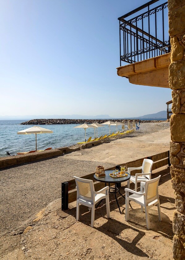 Una terraza frente al mar con sillas y una mesa blancas, con vistas al océano y a la costa rocosa.