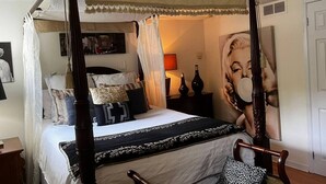 A four-poster canopy bed with a white canopy, a large poster on the wall, and a bedside table with a lamp.