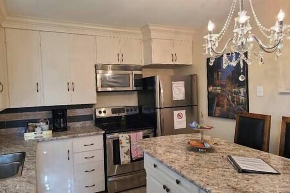A kitchen with white cabinets, stainless steel appliances, a granite countertop, and a chandelier.