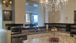A modern kitchen with a granite countertop, stainless steel appliances, and a chandelier.