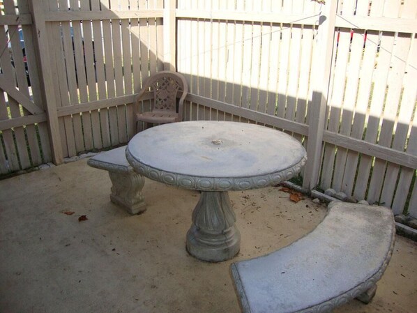 Un patio con una mesa redonda y dos bancos, rodeado por una valla de madera blanca.