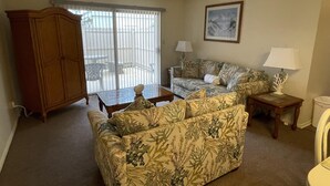 A living room with a sofa, a wooden cabinet, a table, and a chair. - Horizon South 12C4: 1 BR / 1 BA condo in Panama City Beach, Sleeps 4 (Panama City Beach)