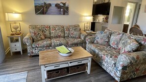 Una sala de estar con un sofá floral, una mesa de centro de madera y un cuadro de una playa.
