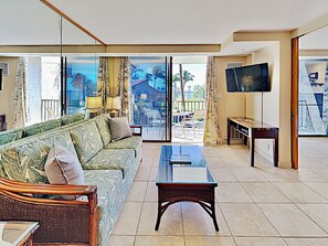 A modern living room with a sofa, a glass coffee table, and a TV. - Fully Upgraded Kihei Condo Sweeping Ocean Views Private Lanai Pool Hot Tub (Kihei)