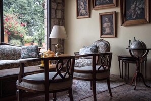 Une pièce chaleureuse avec un canapé, deux chaises en bois, une table avec une lampe et des œuvres d’art encadrées accrochées au mur.