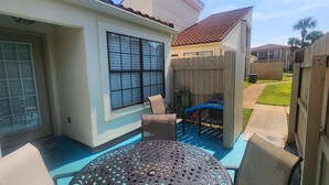 A patio with a table and chairs, a wooden fence, and a window with blinds.