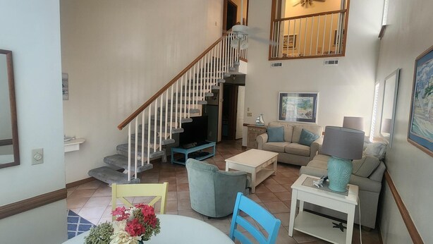 A spacious living area with a staircase, a sofa set, a coffee table, and a dining table with flowers.