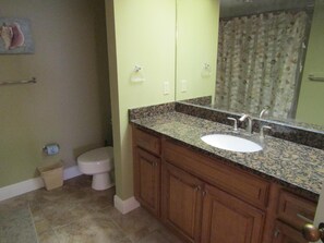 Un baño con lavamanos de encimera de granito, armarios de madera, inodoro y cortina de ducha.