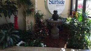 A sign for Surfside Resort with a decorative fountain and lush greenery.