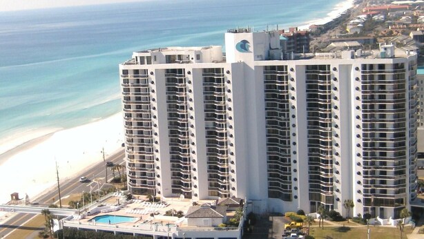 A high-rise hotel with multiple balconies, a pool area, and a beach view.