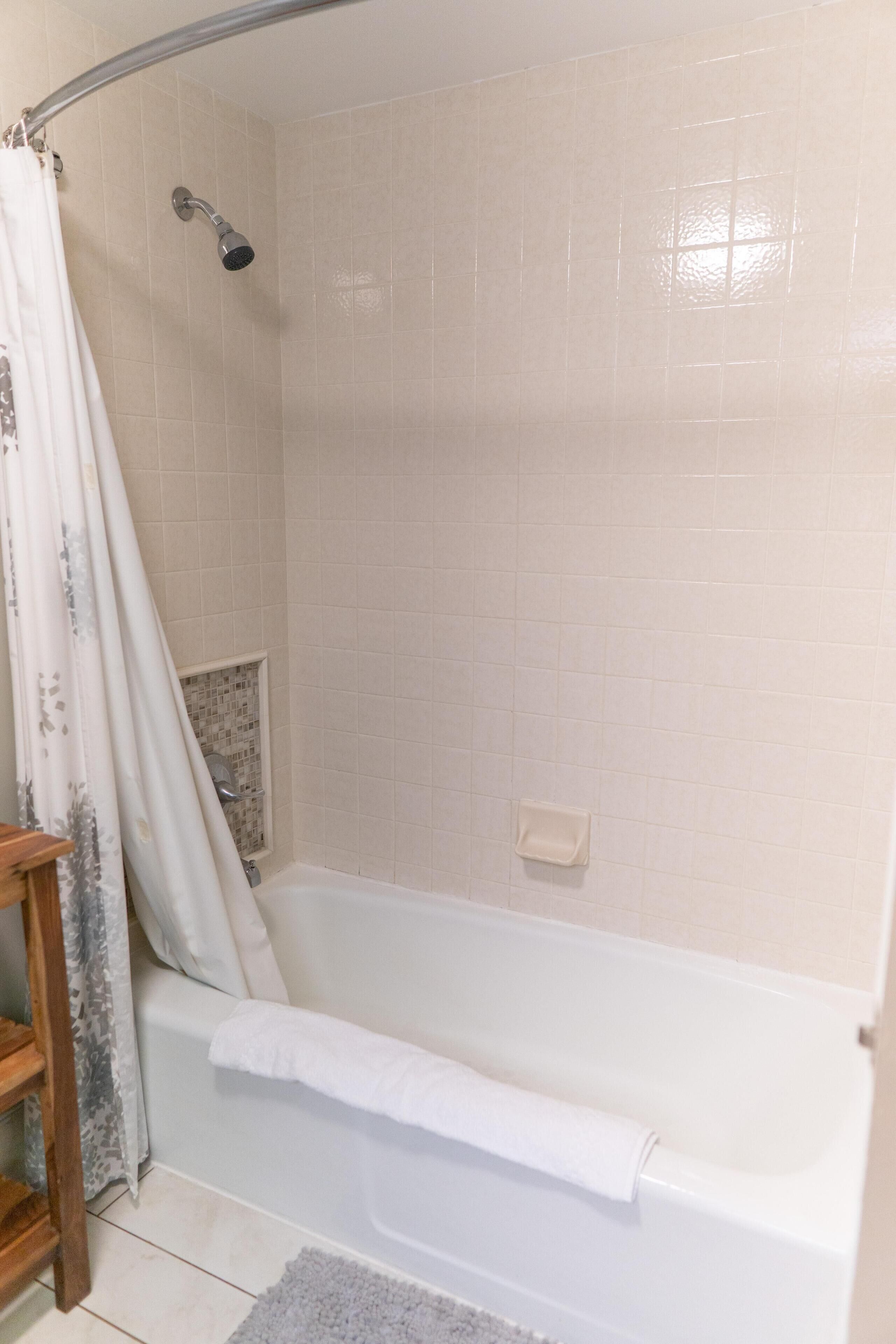 A bathroom with a bathtub, a showerhead, and a tiled wall.