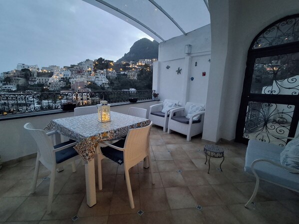 A balcony with a table and chairs, a lantern, and a view of a hillside town.