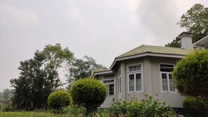 A house with a well-maintained lawn, a small garden with flowers, and a large tree in the background.