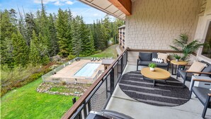 A balcony with a pool, outdoor seating, and a view of a forested area.