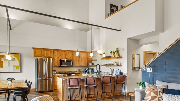 A spacious living area with a wooden ceiling, a kitchen with modern appliances, and a cozy seating area with a sofa and chairs.