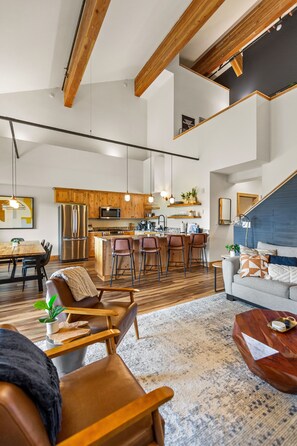 A spacious living area with a wooden ceiling, a kitchen with modern appliances, and a cozy seating area with a sofa and chairs. - THE CLYDE (Clackamas County)