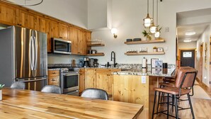 A modern kitchen with wooden cabinets, stainless steel appliances, and a large wooden dining table.