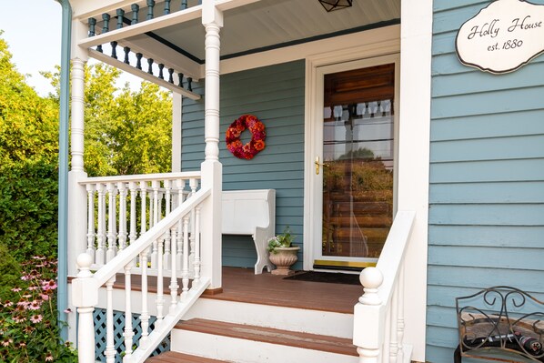 A porch with a white railing, a wooden staircase, a door with a glass panel, and a wreath on the wall.