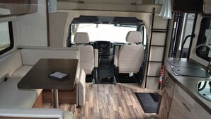 A compact RV interior with a dining area, kitchenette, and seating.