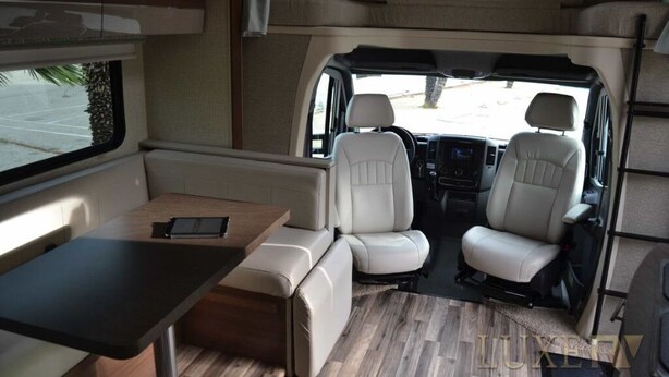 A compact RV interior with a kitchenette, two seating areas, and a small table.