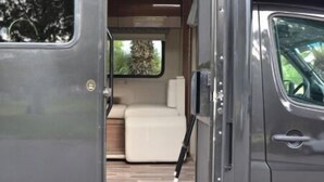 A luxury RV interior with a bed, a small seating area, and a window.