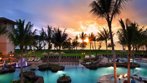 A resort pool area with lounge chairs, palm trees, and a sunset view.