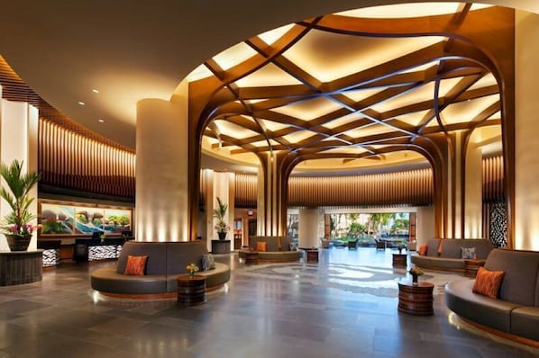 Un hall d’entrée spacieux au design moderne, doté d’un plafond incurvé avec des poutres en bois et d’un espace salon avec des canapés et une table basse.