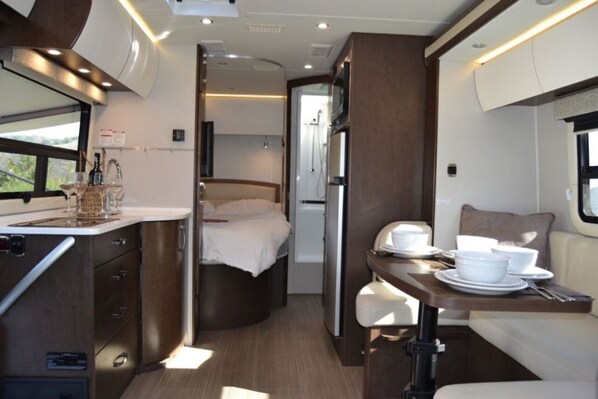 A compact RV interior with a kitchenette, a bed, and a dining area.