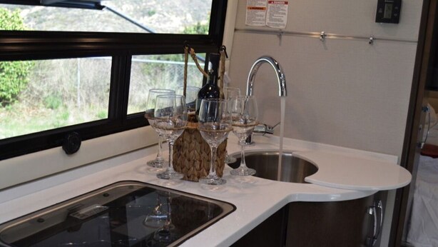 Una cocina con un lavamanos, una ventana y una botella de vino.